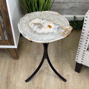May include: A white agate end table with a black metal base. The table top is a natural slice of agate with a unique pattern.