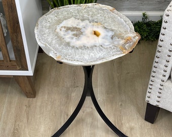 May include: A white agate end table with a black metal base. The table top is a natural slice of agate with a unique pattern.