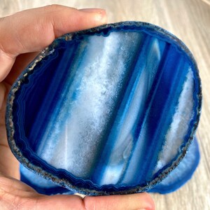 May include: Blue agate coaster with white and blue banding. The coaster is round and has a polished edge.