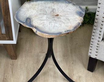 May include: A white agate slice table top with a black metal tripod base. The agate slice has a natural, organic shape and a light grey and white colour.
