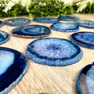 May include: A collection of blue agate coasters with a white center and a dark blue rim. The coasters are arranged in a row on a wooden surface.