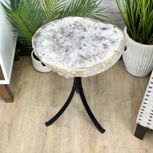 May include: A white agate slice end table with a black metal tripod base. The table is on a light wood floor.
