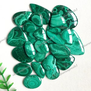 May include: A collection of polished malachite gemstones in various shapes, including ovals, teardrops, and irregular forms. The stones display a rich, deep green color with swirling patterns and textures. The image is taken from a high angle, showcasing the natural beauty of the stones.