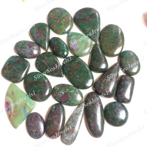 May include: A collection of polished gemstones in various shapes, including oval, teardrop, and irregular forms. The stones feature a deep green base color with red and pink inclusions, creating a marbled effect. The gemstones are arranged closely together.