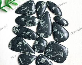 May include: A collection of polished, dark green gemstones with white, crystalline inclusions. The stones are various shapes, including teardrop, oval, and rectangular. The image is well-lit, showcasing the natural patterns and textures of the stones.