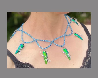 May include: A blue beaded necklace with iridescent green beetle wing pendants. The necklace has a delicate, layered design and is accented with silver wire.