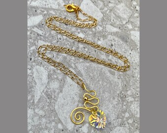 May include: A gold chain necklace with a heart-shaped crystal pendant. The pendant is attached to a gold wire that is twisted into a decorative design.