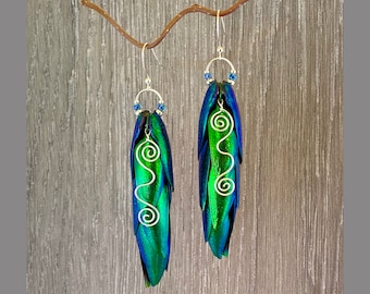 May include: A pair of dangle earrings featuring iridescent green beetle wings with silver wire accents and blue crystal beads.