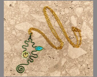 May include: A gold chain necklace with a green wire pendant featuring a stylized flower and leaf design. The pendant is made of wire and has a blue and white flower.