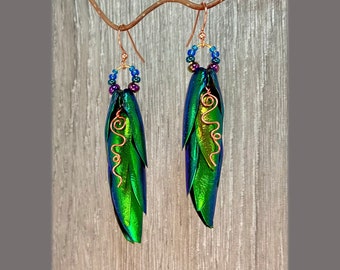 May include: A pair of iridescent green earrings with copper wire accents and blue and purple beads. The earrings are shaped like beetle wings.