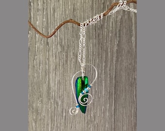 May include: A silver chain necklace with a green and blue iridescent beetle wing pendant. The pendant is wrapped in silver wire and has small blue beads.