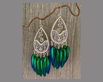 May include: Silver dangle earrings with a filigree design and green iridescent beetle wing accents.