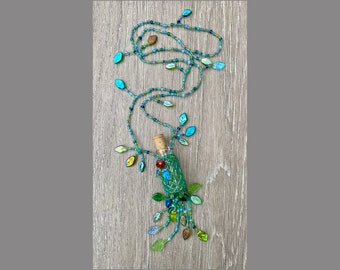 May include: A decorative glass bottle wrapped in green mesh, adorned with a cork stopper and colorful beads. A beaded vine with leaf-shaped beads in shades of blue, green, and brown extends from the bottle, creating a whimsical, nature-inspired design.