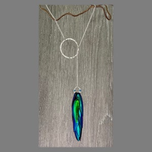 Puede incluir: Un collar de cadena de plata con un colgante circular y un colgante largo y colgante hecho de alas de escarabajo iridiscentes verde y azul.