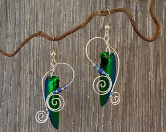 May include: A pair of silver earrings with green iridescent beetle wing pieces and blue beads. The earrings have a delicate, swirling wire design.