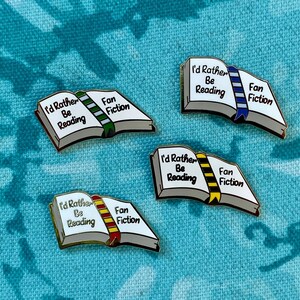May include: Four enamel pins in the shape of open books, each with the text "I'd Rather Be Reading" and "Fan Fiction." The book spines are colored green, blue, yellow, and red. The pins have a gold border and are set against a teal patterned background.