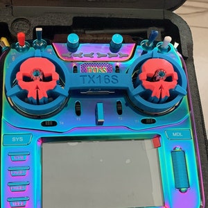 Peut inclure: Un émetteur radiocommande noir et iridescent avec un écran couleur, un motif de crâne sur les boutons et le texte "TX16S" sur le devant.