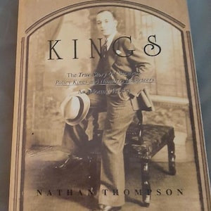 May include: A vintage book cover with a black and white photo of a man in a suit and hat. The title of the book is "Kings: The True Story of Chicago Policy Kings and Numbers Racketeers, An Informal History" by Nathan Thompson.