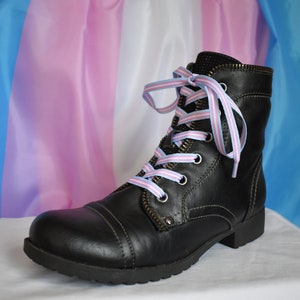May include: Black leather boots with laces tied in the colors of the transgender pride flag, blue, pink, and white.