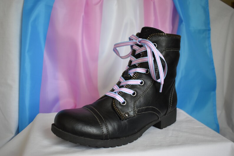 May include: Black leather boots with laces tied in the colors of the transgender pride flag, blue, pink, and white.