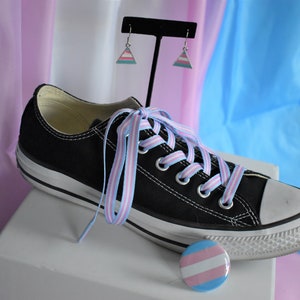 May include: Black Converse sneakers with light blue and pink striped shoelaces, a transgender pride pin, and a pair of transgender pride triangle earrings.