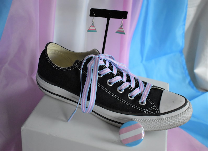 May include: Black Converse sneakers with light blue and pink striped shoelaces, a transgender pride pin, and a pair of transgender pride triangle earrings.