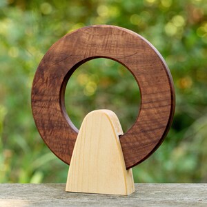 May include: A wooden sculpture with a circular opening in the center. The sculpture is made of two pieces of wood, one dark brown and one light brown. The dark brown piece is shaped like a ring and the light brown piece is shaped like a triangle.