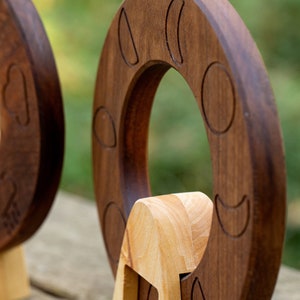 May include: Two wooden moon phase rings with a carved design of the moon in different phases. The rings are made of dark brown wood and light brown wood.