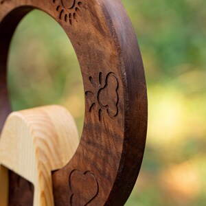 May include: A wooden toy with a circular shape and a carved design of a sun, a cloud, and a heart. The toy is made of two different types of wood, one light and one dark.