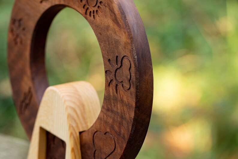 May include: A wooden toy with a circular shape and a carved design of a sun, a cloud, and a heart. The toy is made of two different types of wood, one light and one dark.