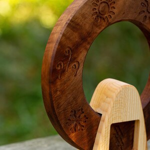 May include: A wooden ring with intricate carvings of a sun, a heart, and a snowflake. The ring is mounted on a wooden stand.