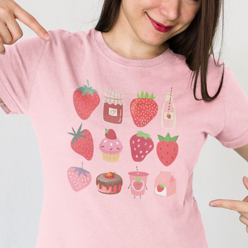 Puede incluir: Camiseta rosa claro con un dise&ntilde;o de fresas. El dise&ntilde;o incluye ilustraciones de fresas, mermelada de fresa, una magdalena, una tarta de chocolate, una bebida de fresa y un cart&oacute;n de leche con una fresa.