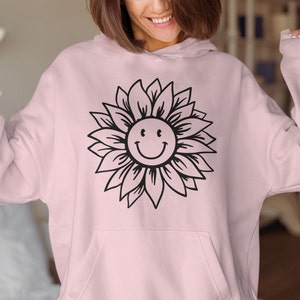May include: A pink hoodie with a black outline of a sunflower with a smiley face in the center.