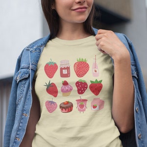 Puede incluir: Camiseta color crema con un dise&ntilde;o de fresas. El dise&ntilde;o incluye ilustraciones de fresas, mermelada de fresa, una magdalena, una tarta de chocolate, una bebida de fresa y un cart&oacute;n de leche de fresa.