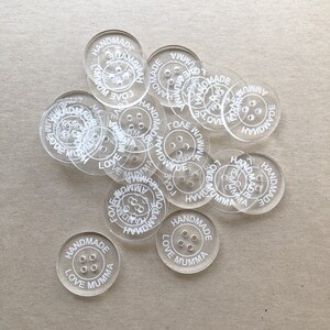 May include: A pile of clear plastic buttons with the text "Handmade Love Mumma" printed on them.