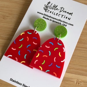 May include: Red heart-shaped earrings with a colourful sprinkle pattern. The earrings are made of acrylic and have green glitter accents. The earrings are on a white card with the text "little dream collection" and "www.littledreamcollection.com Made in Ipswich, Qld".