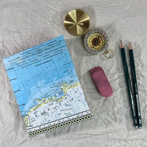 Handmade journal with a partial map of Antartica on the front cover. Next to the journal is an eraser, two pencils, and a compass.