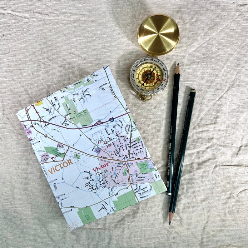 Handmade journal with a map of Victor, New York on the front cover. Next to the journal is two pencils and a compass.