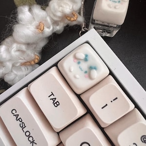May include: A white keyboard with a white keycap featuring a cartoon bunny face with blue and pink accents. The keycap is labeled "TAB". The keyboard also has keys labeled "CAPSLOCK", "Q", "1", and "2".
