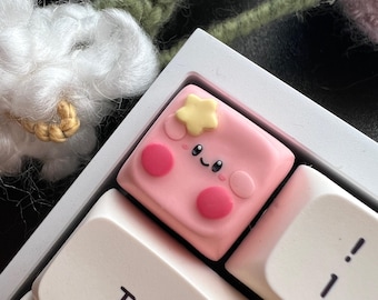 May include: A pink keycap with a cute cartoon face and a yellow star on top. The keycap is labeled "TAB" and is on a white keyboard.