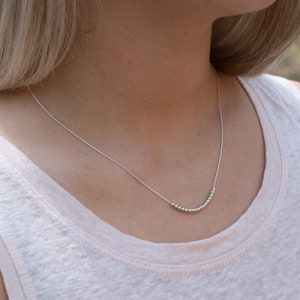 May include: A silver necklace with a row of small silver beads in a curved shape.