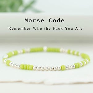 May include: A delicate bracelet with lime green and silver beads. The text "Morse Code" and "Remember Who the Fuck You Are" is above the bracelet. The bracelet is on a white surface.