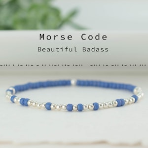 Op de afbeelding: Een armband met blauwe en zilveren kralen. De tekst "Morse Code Beautiful Badass" is zichtbaar. De armband ligt op een witte ondergrond.