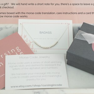 May include: A silver necklace with the word "BADASS" in Morse code is displayed on a white card. The image includes a pink card with the text "cursing -n code" and a gray gift box. The text on the card explains how Morse code works.