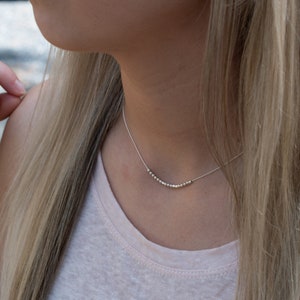 May include: A silver necklace with a delicate chain and a row of small silver beads.