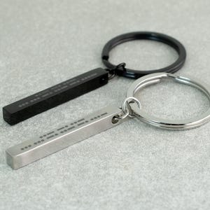 May include: Two silver keychains with black rings. One keychain has a black bar with braille lettering and the other has a silver bar with braille lettering.