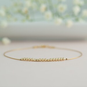 May include: A delicate gold chain bracelet with a row of small gold beads and a few gold cylinders.