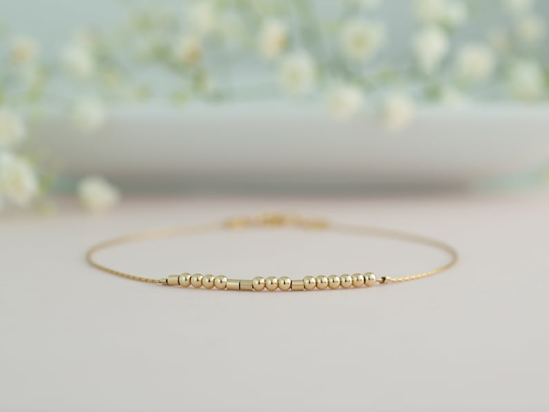May include: A delicate gold chain bracelet with a row of small gold beads and a few gold cylinders.