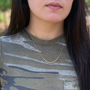 May include: A gold beaded necklace on a person wearing a camouflage shirt.