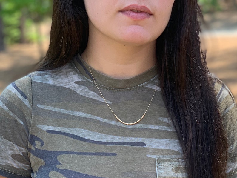 May include: A gold beaded necklace on a person wearing a camouflage shirt.